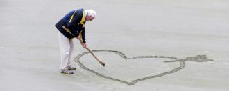 Elderly man drawing a heart in the sand